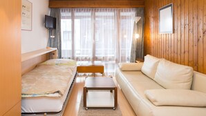 Een kleine hotelkamer met een bed, een slaapbank, een tafeltje en een televisie.