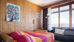 Um quarto acolhedor com cama, sofá, parede de madeira, janela com vista e um quadro de uma árvore.