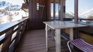 Um deck de madeira com mesa e cadeiras, uma porta de vidro do chuveiro e vista para montanhas cobertas de neve.