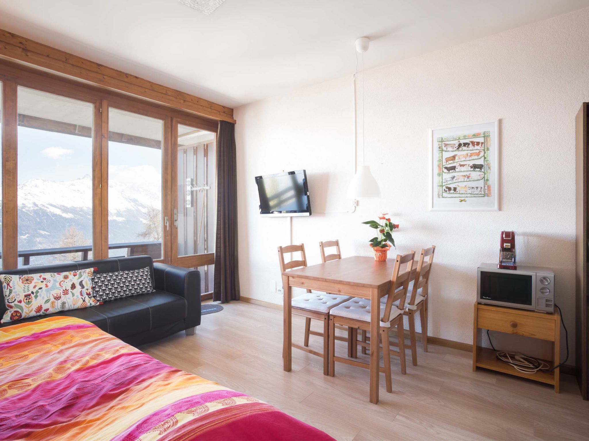 A room with a bed, a sofa, a dining table with chairs, a TV, and a small cabinet.