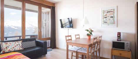 A room with a bed, a sofa, a dining table with chairs, a TV, and a small cabinet.
