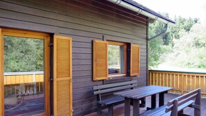 A wooden cabin with a deck, two windows with shutters, and a picnic table. - Fischerhütte by Interhome (Stein an der Enns)