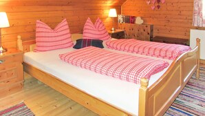 A cozy wooden cabin bedroom with two single beds, a nightstand with a lamp, a dresser, and a wall decorated with heart-shaped ornaments. - Fischerhütte by Interhome (Stein an der Enns)