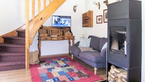 A cozy living room with a wooden staircase, a fireplace, a television, and a patterned rug. - Fischerhütte by Interhome (Stein an der Enns)