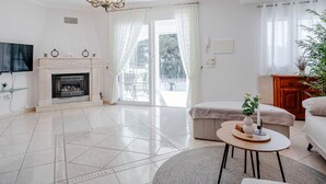 A modern living room with a fireplace, a chandelier, a television, and a large window with curtains. - Heringklee by Interhome (Calpe/Calp)