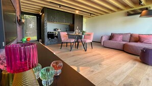 A modern interior with a wooden ceiling, a dining area with pink chairs, a sofa, and a kitchen in the background. - Romantic Stay with Views (Enneille)