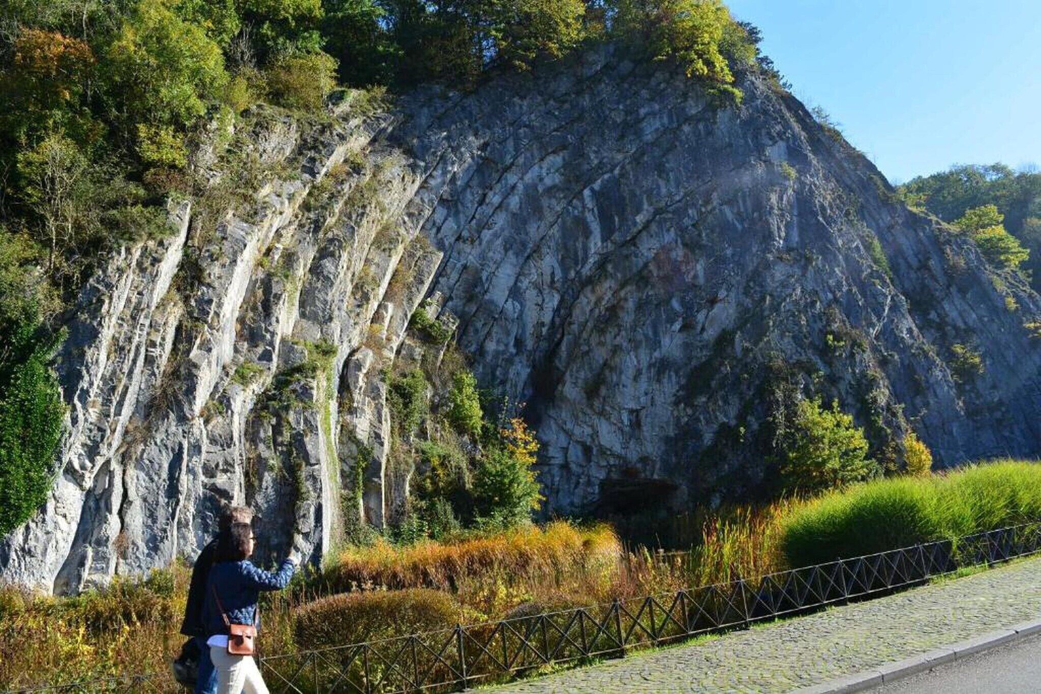 Une falaise rocheuse avec un sentier pavé et une clôture en métal.