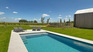 A rectangular swimming pool with clear blue water, surrounded by a well-maintained lawn and a few trees. - Cozy Romantic Stay Near Durbuy (Enneille)