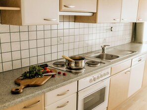 Een keuken met witte kastjes, een betegelde spatwand, een fornuis, een spoelbak en een snijplank met groenten.