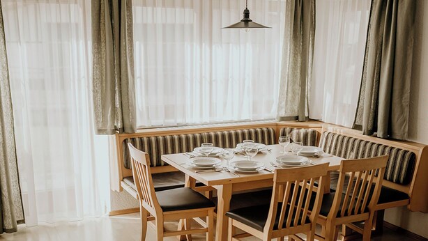 A dining area with a wooden table set for four, surrounded by cushioned benches.