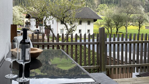 A balcony with a table, wine glasses, and a bottle, overlooking a wooden fence and a valley with houses and trees. - Eberharter by Interhome (Zell am Ziller)