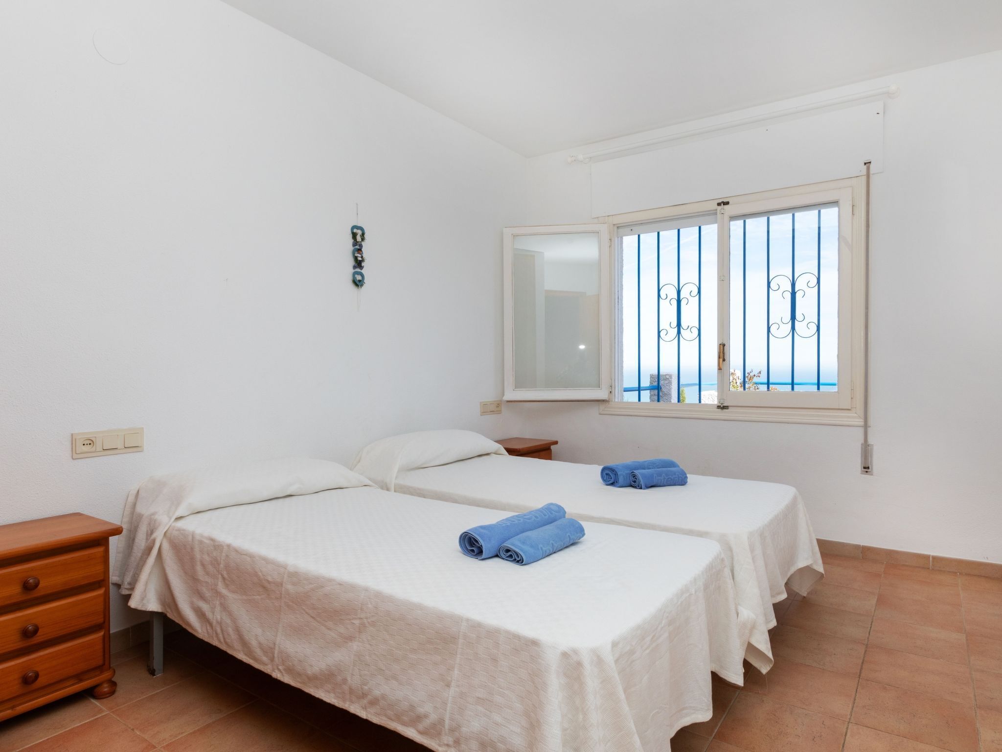 A small, clean room with two beds, a wooden dresser, a mirror, and a window with a view.