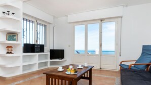 Un salon avec un téléviseur, une table avec des tasses et une assiette, un canapé et une vue sur la mer.