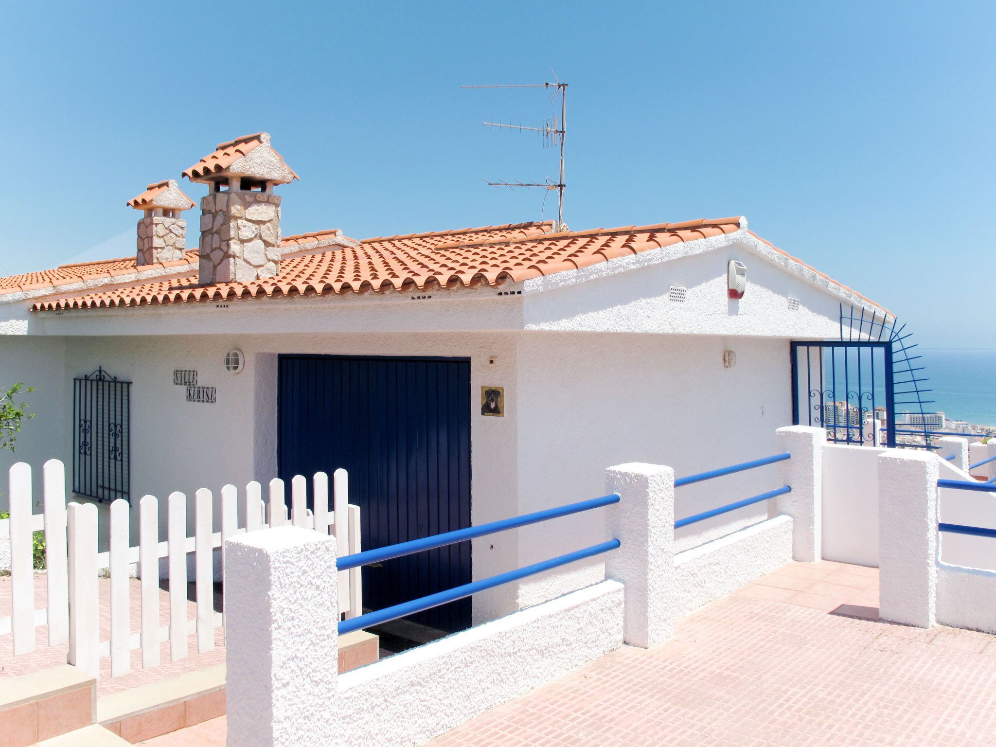 A coastal building with a tiled roof, a blue door, and a white fence.
