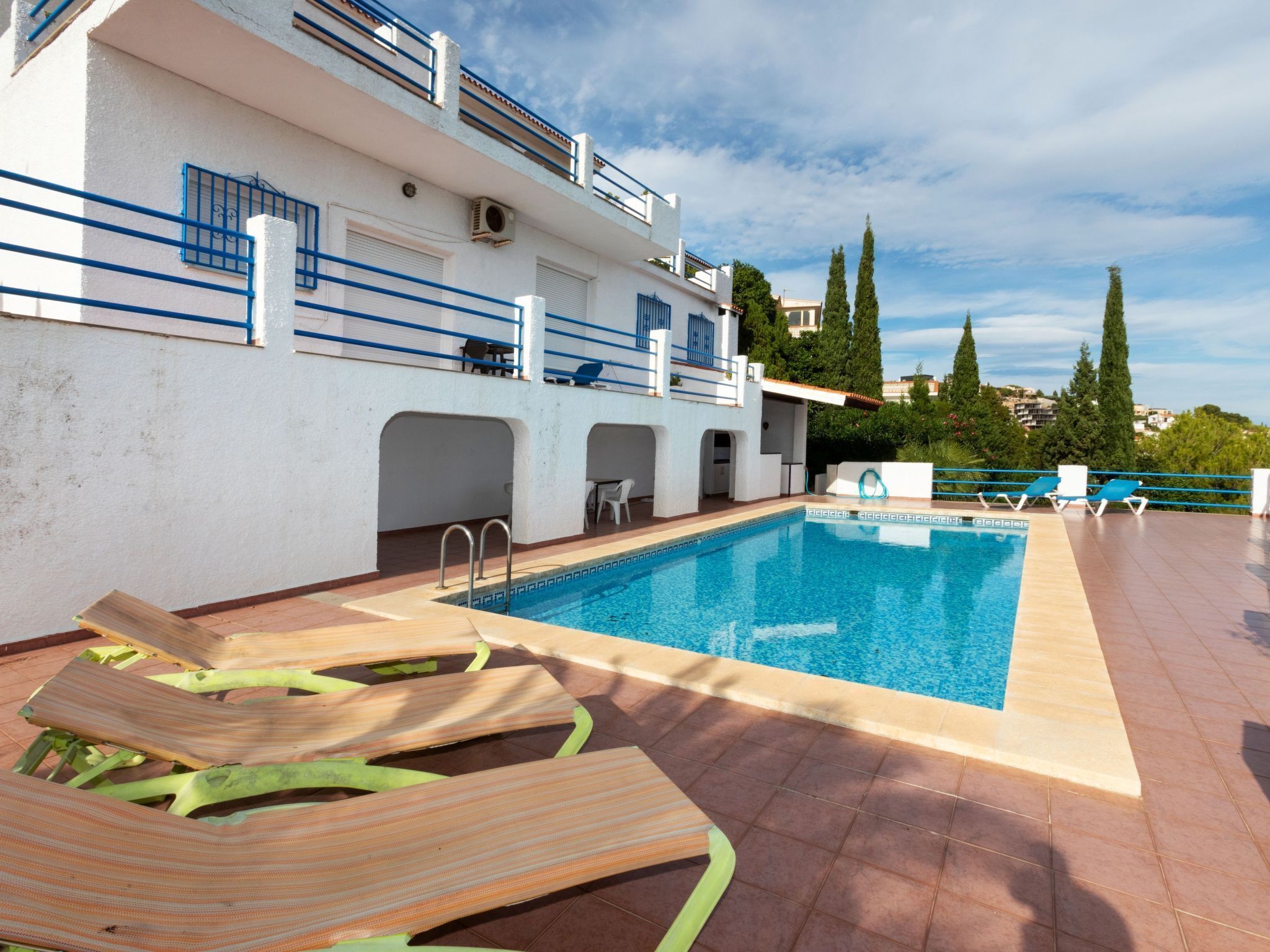 Une piscine avec des chaises longues, un bâtiment doté de balcons et un ciel dégagé.