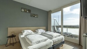 Een moderne hotelkamer met een groot bed, een klein nachtkastje en een balkon met uitzicht op de stad.