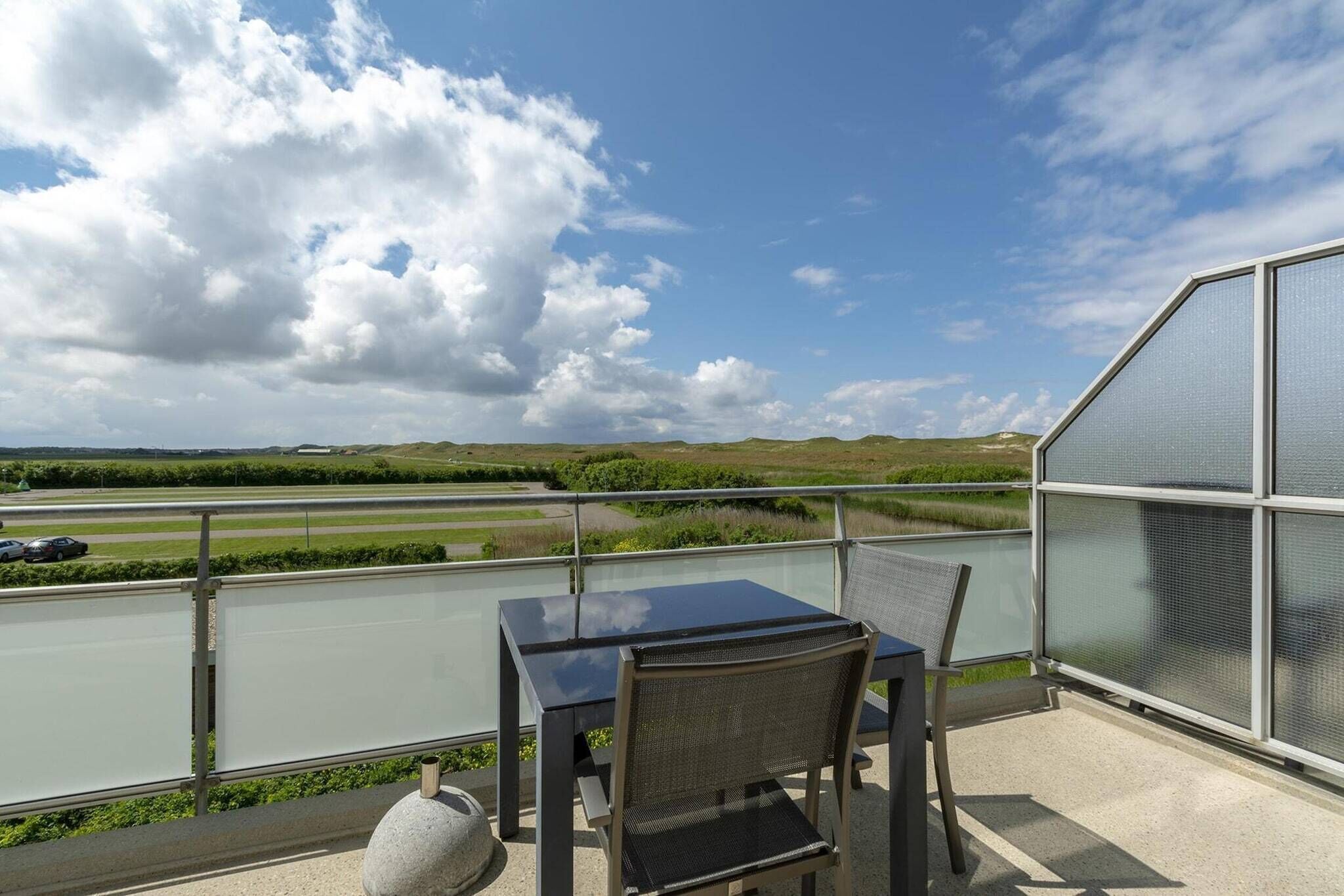 A balcony with a table and chairs, overlooking a road and greenery.