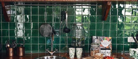 A kitchen with a green tiled backsplash, stainless steel sink, and various kitchen utensils and jars.