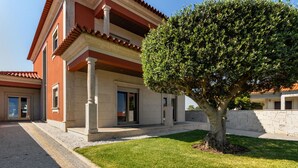 Un edificio de dos plantas con un porche cubierto, un muro de piedra y un césped cuidado.
