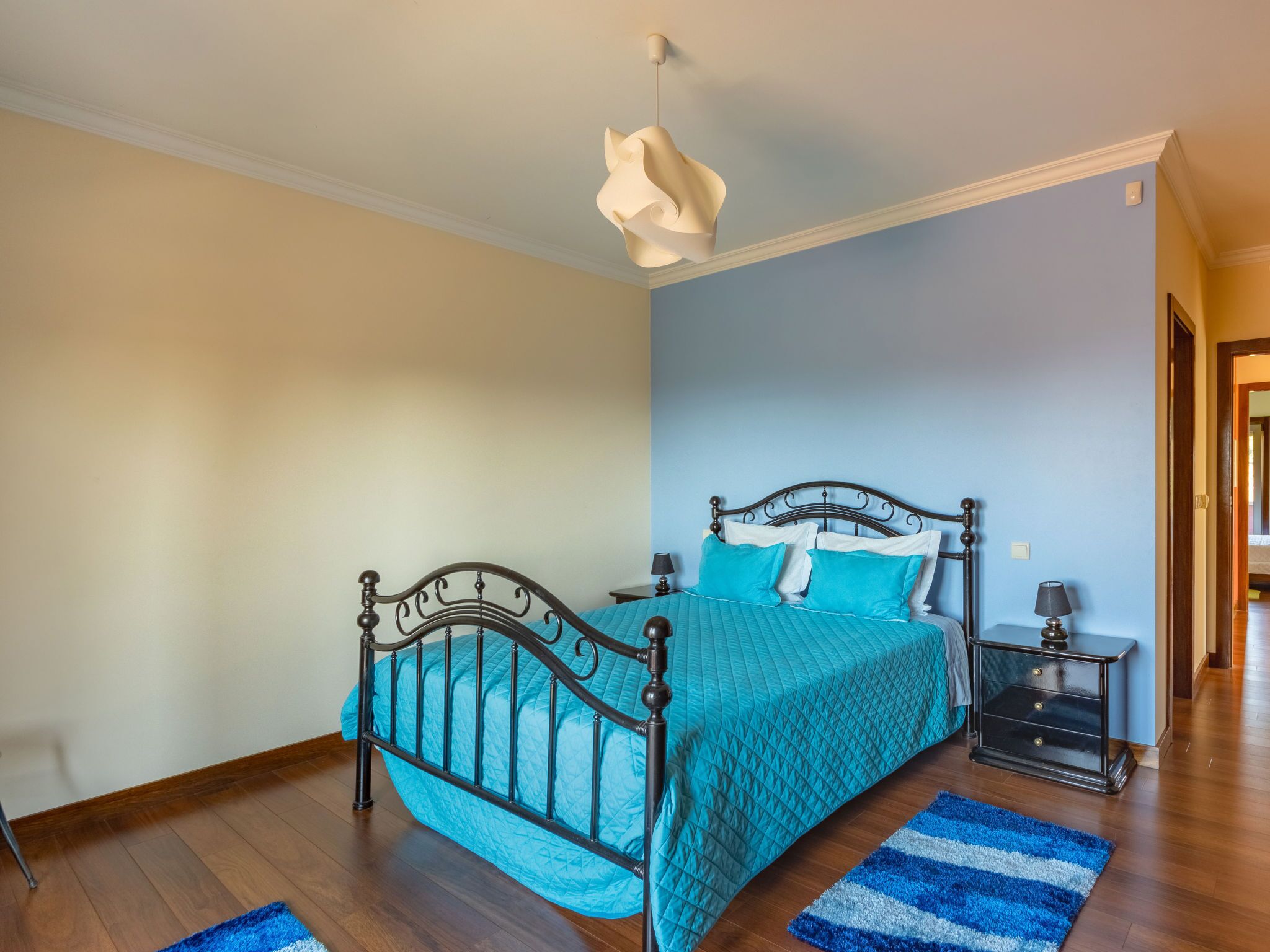 Ein Schlafzimmer mit einem Bett, einem Nachttisch, einer Lampe, einem blau-weiß gestreiften Teppich und einer Pendelleuchte.