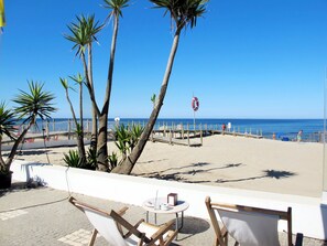 A beachside patio with wooden chairs and a small table, overlooking the ocean.