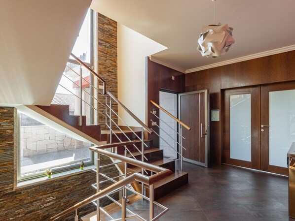 A modern interior with a wooden staircase, a stone accent wall, and a view through a large window.