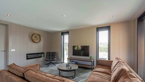 A modern living room with a sofa, a coffee table, a TV, and a fireplace. - Villa near North Holland Beach with Jacuzzi (Julianadorp aan Zee)