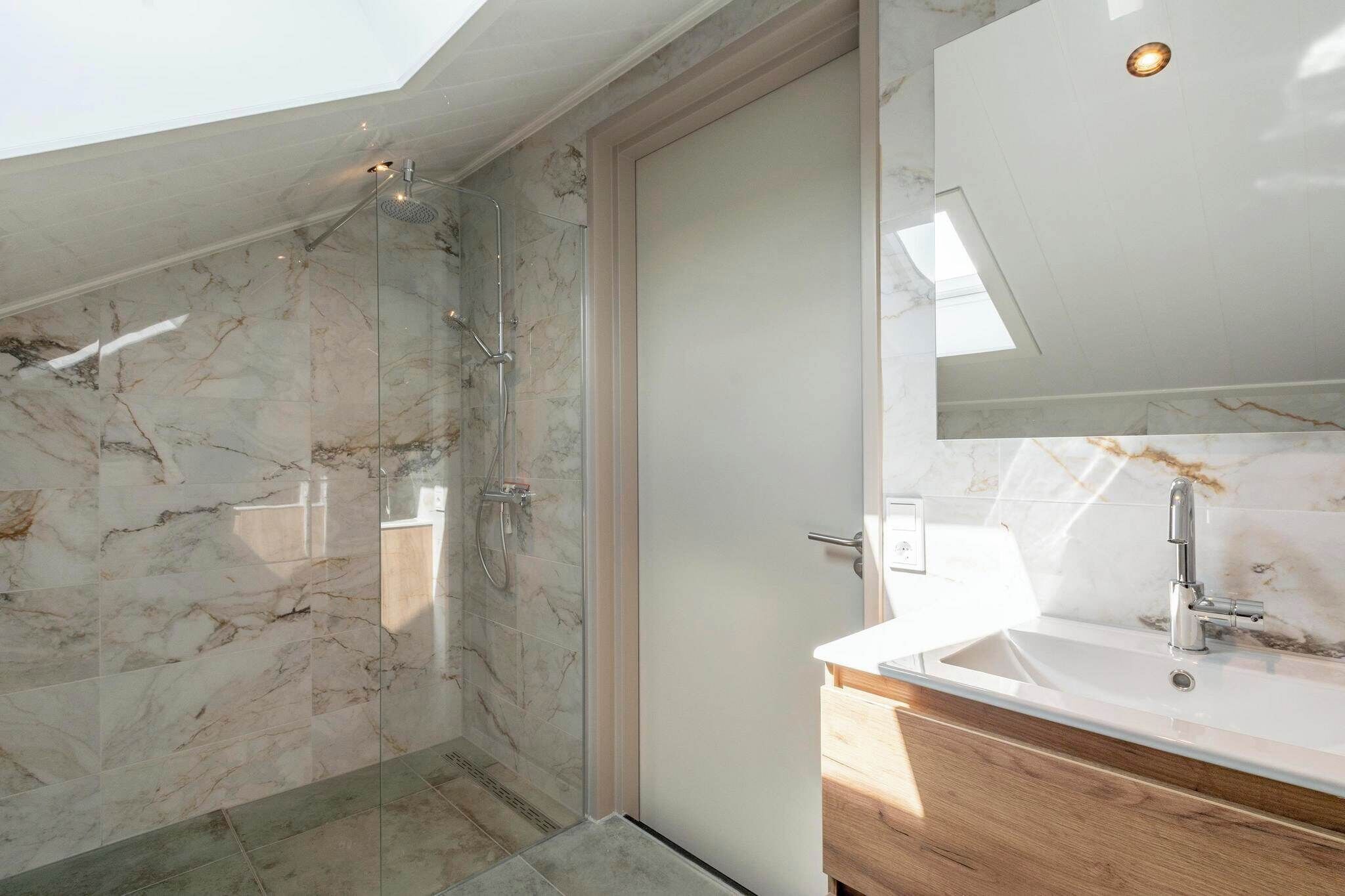 Un baño moderno con ducha de vidrio, paredes de mármol y tocador de madera con lavamanos blanco.