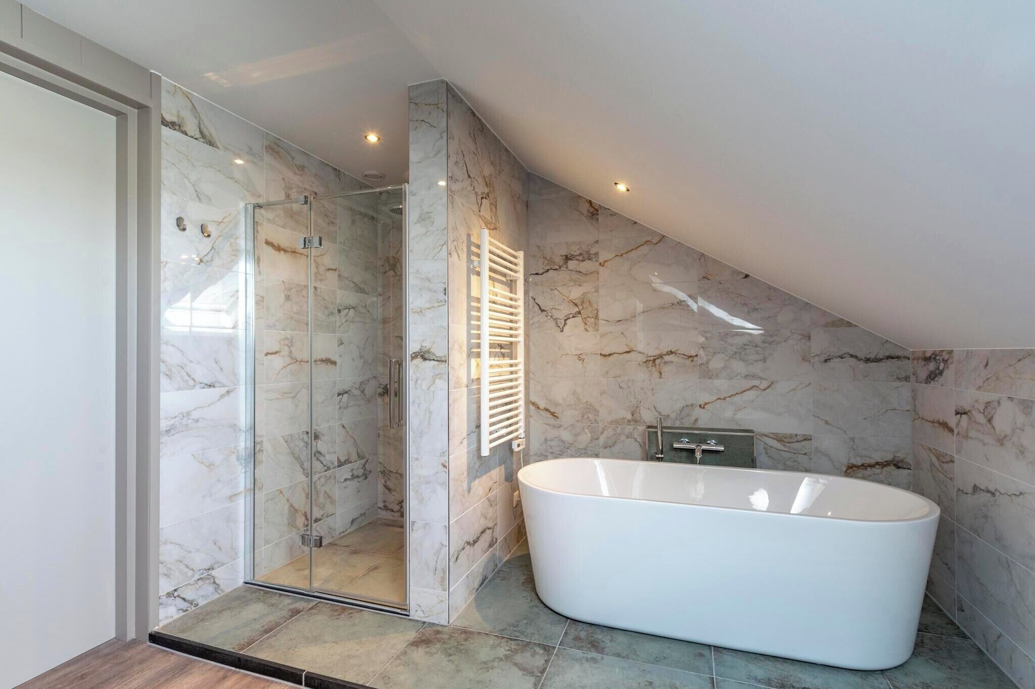 Een moderne badkamer met een douchecabine van glas, een vrijstaand bad en marmeren wanden.