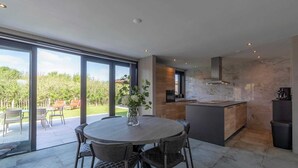 A modern kitchen with a marble backsplash, a dining area with a round table and chairs, and large sliding glass doors leading to a patio with outdoor furniture. - Villa near North Holland Beach with Jacuzzi (Julianadorp aan Zee)