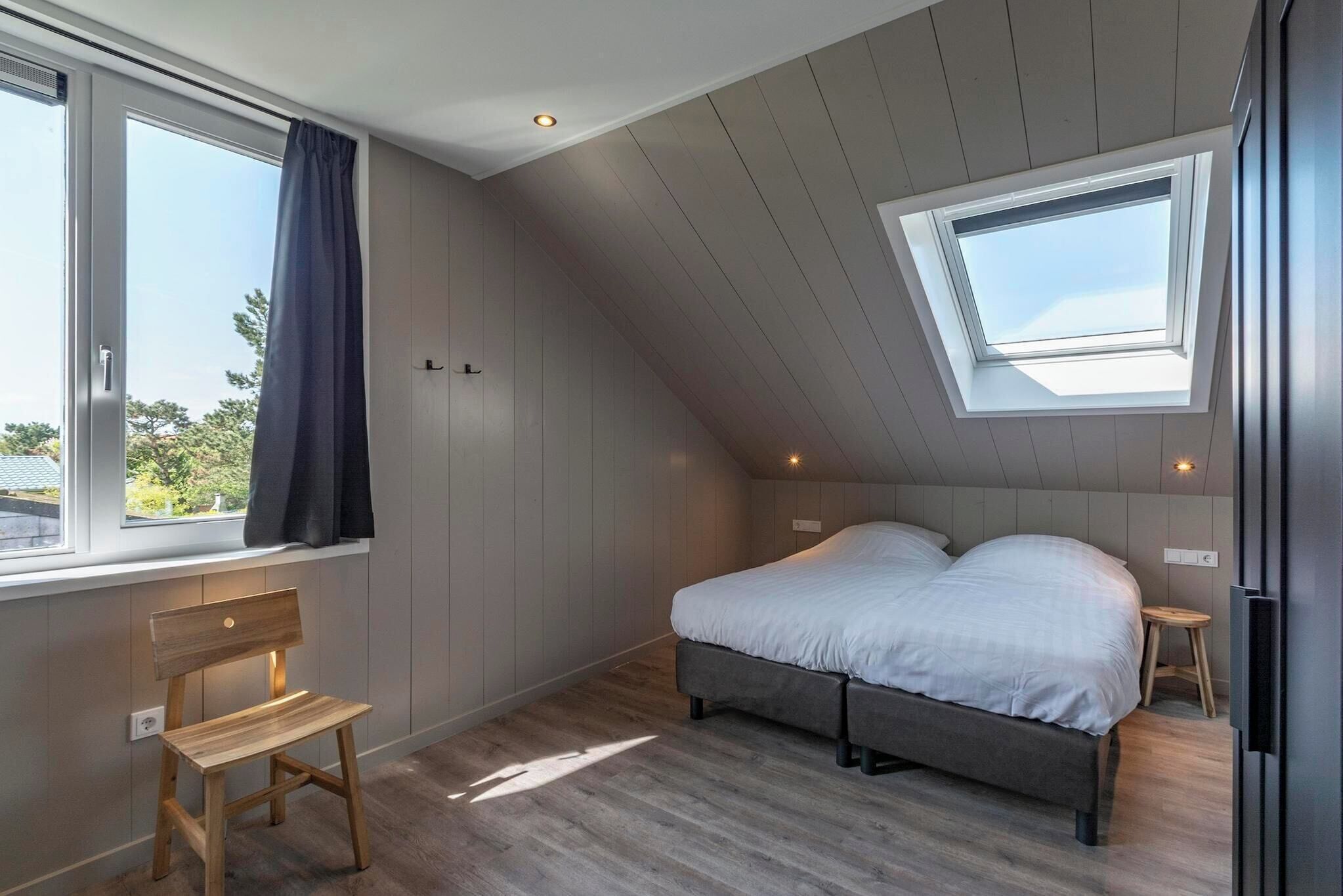 A bedroom with a sloped ceiling, a skylight, a bed, a chair, and a small stool.