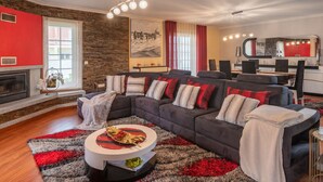 Un salon moderne avec un canapé d’angle, une cheminée, un coin repas et une cuisine en arrière-plan.