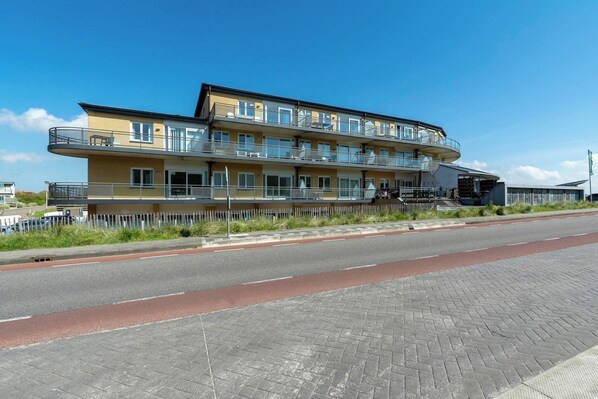 A multi-story hotel with balconies, a paved walkway, and a clear sky.