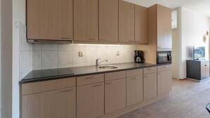 A modern kitchen with light wood cabinets, a black countertop, and a built-in oven.
