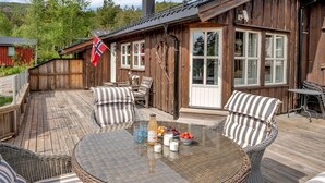 Une terrasse en bois avec des meubles en osier, une table avec des boissons et un drapeau.