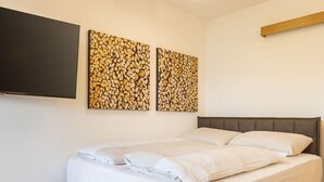Una cama bien tendida con sábanas blancas, cabecera gris y dos cuadros en la pared con texturas de madera.