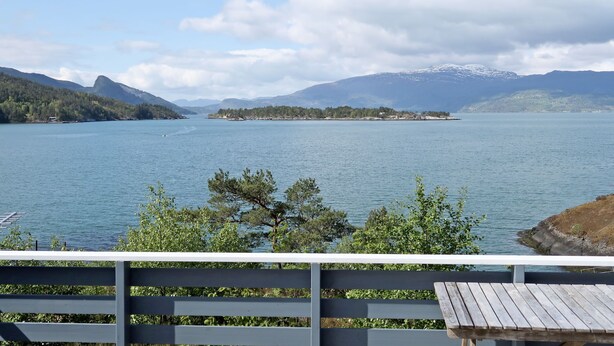 Une vue sur le lac, avec une terrasse en bois, un ciel dégagé et des montagnes à l’horizon.
