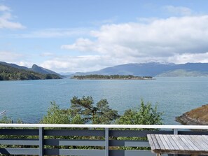 Vista de un lago con muelle de madera, cielo despejado y montañas a lo lejos.