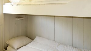 Un lit superposé avec un matelas et des oreillers blancs, une tête de lit blanche et un lambris en bois.