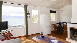 Un salon confortable avec un téléviseur, un coin repas avec une table et des chaises, une cuisine équipée d’un réfrigérateur et une cheminée.