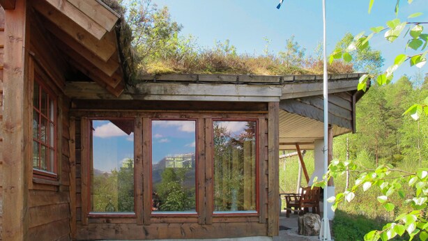 Une cabane en bois dotée de grandes fenêtres, d’un drapeau et d’un toit végétalisé.