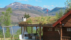 Une cabane en bois avec un petit porche et un mât pour drapeau, offrant une vue sur un lac et des montagnes.