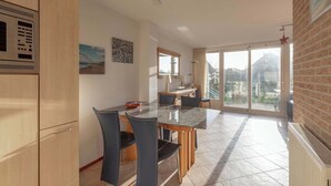 A modern kitchen with a built-in microwave, a dining area with a glass table and chairs, and a large sliding glass door leading to a balcony. - Callantsogervaart 3-8 home near Beach (Julianadorp aan Zee)
