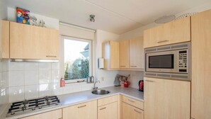 A modern kitchen with light wood cabinets, a stainless steel stove, a microwave, and a window providing natural light. - Callantsogervaart 3-8 home near Beach (Julianadorp aan Zee)