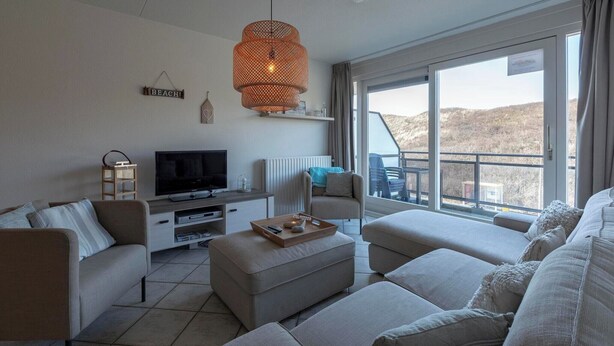 Ein modernes Wohnzimmer mit Fernseher, Sofa, Hocker und einem großen Fenster mit Blick.