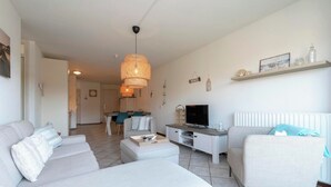 Ein modernes Wohnzimmer mit Sofa, Couchtisch, Fernseher und Essbereich im Hintergrund.