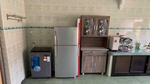 A compact kitchen with a refrigerator, a water dispenser, and a wooden cabinet with decorative glass doors. - OYO 91025 THHomeStay (Bahau)