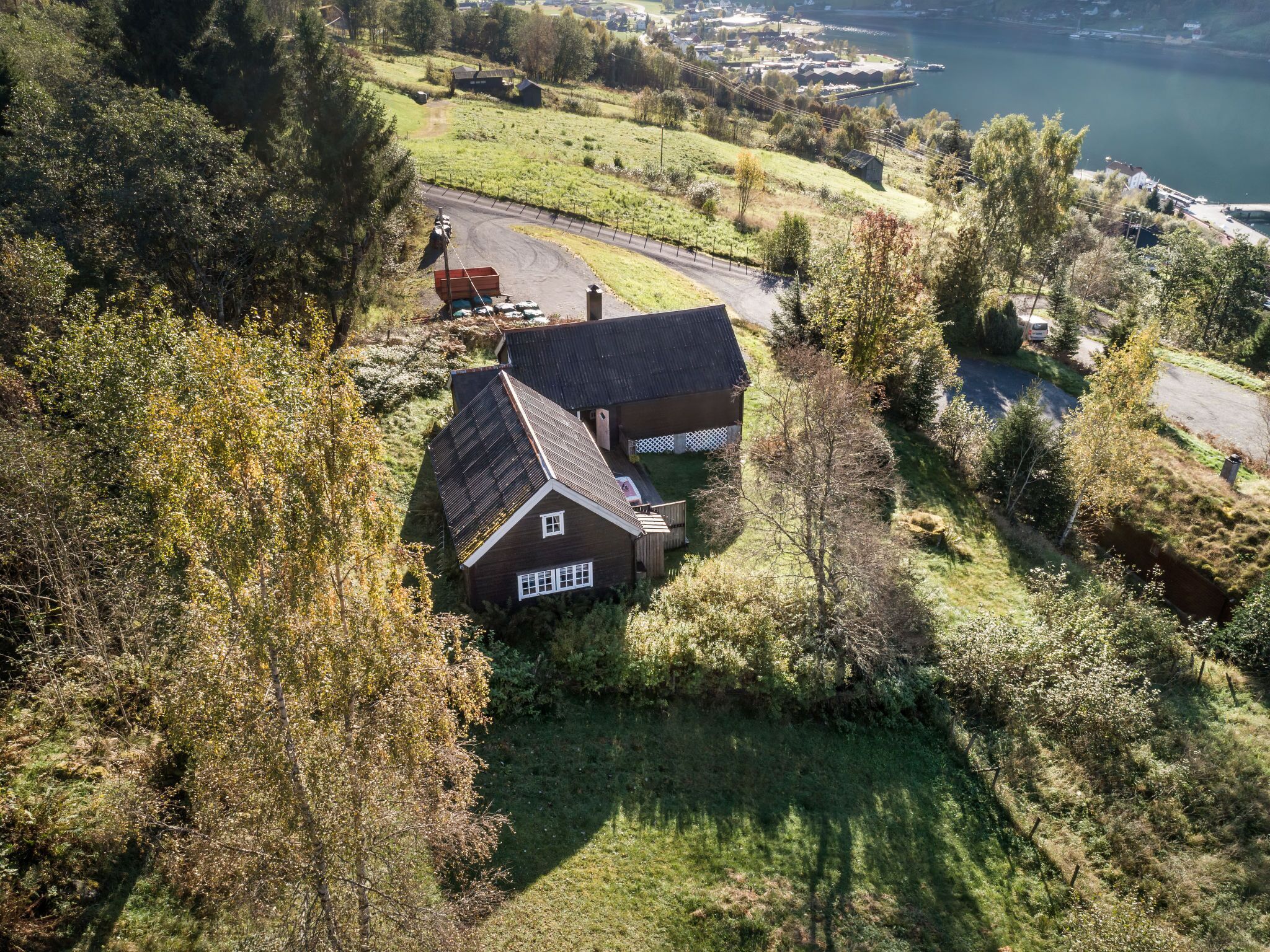 Vue aérienne d’une maison avec un toit en pente, entourée d’une cour clôturée et bordée d’une étendue d’eau en arrière-plan.