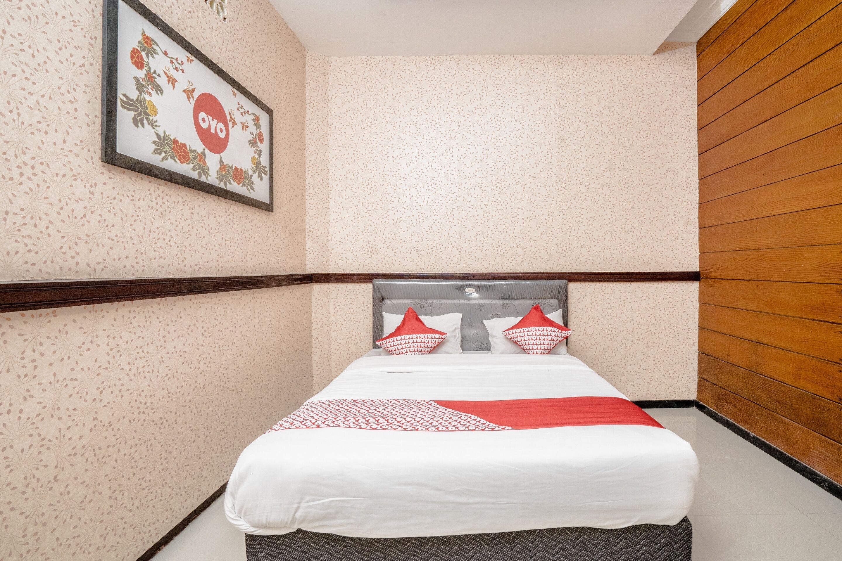 A neatly arranged hotel room with a bed, a framed picture on the wall, and a wooden panel on one side.