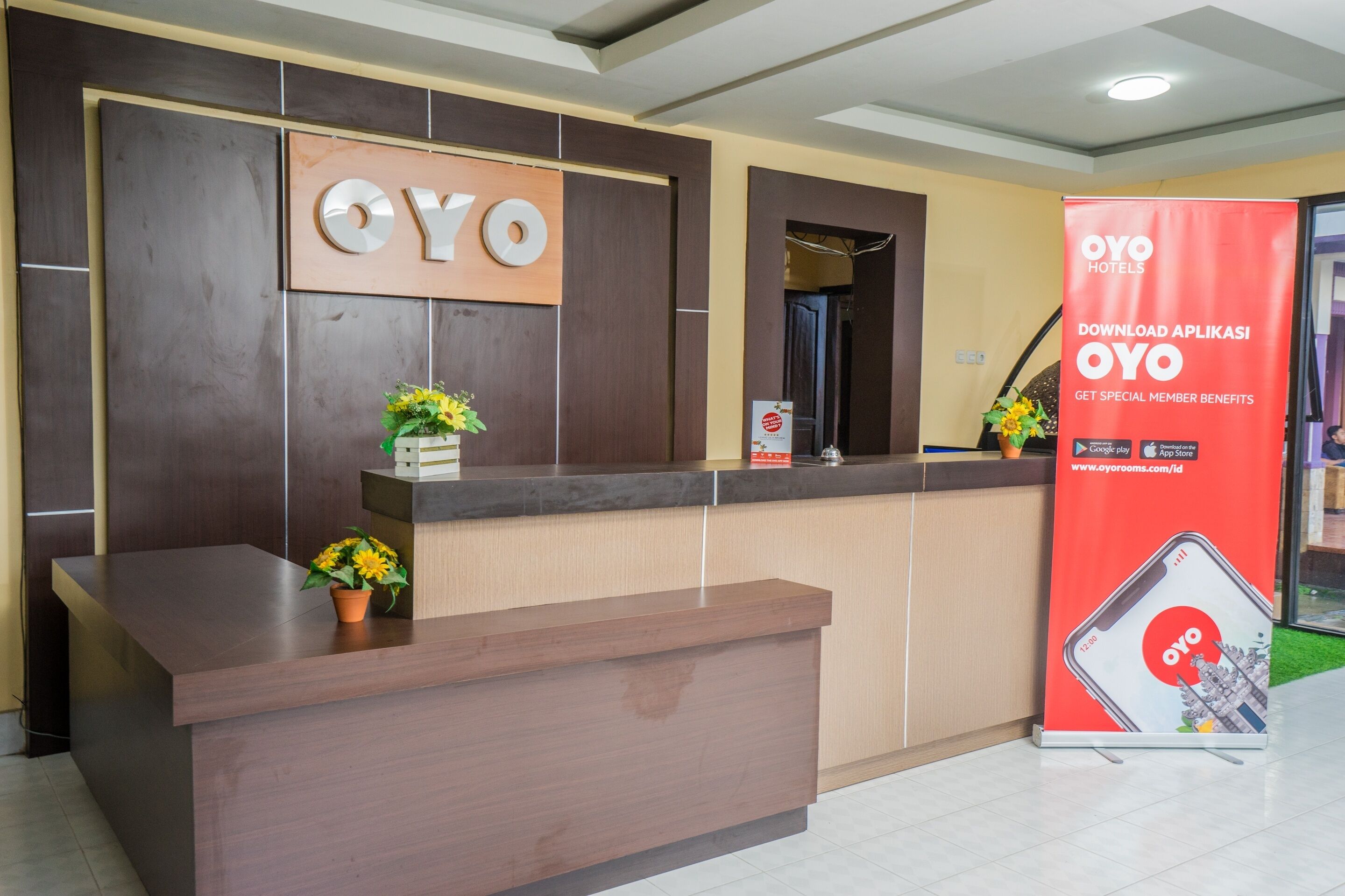 Uma receção com acabamento em madeira, um letreiro com as letras "OYO" na parede e um banner promocional da OYO Hotels.